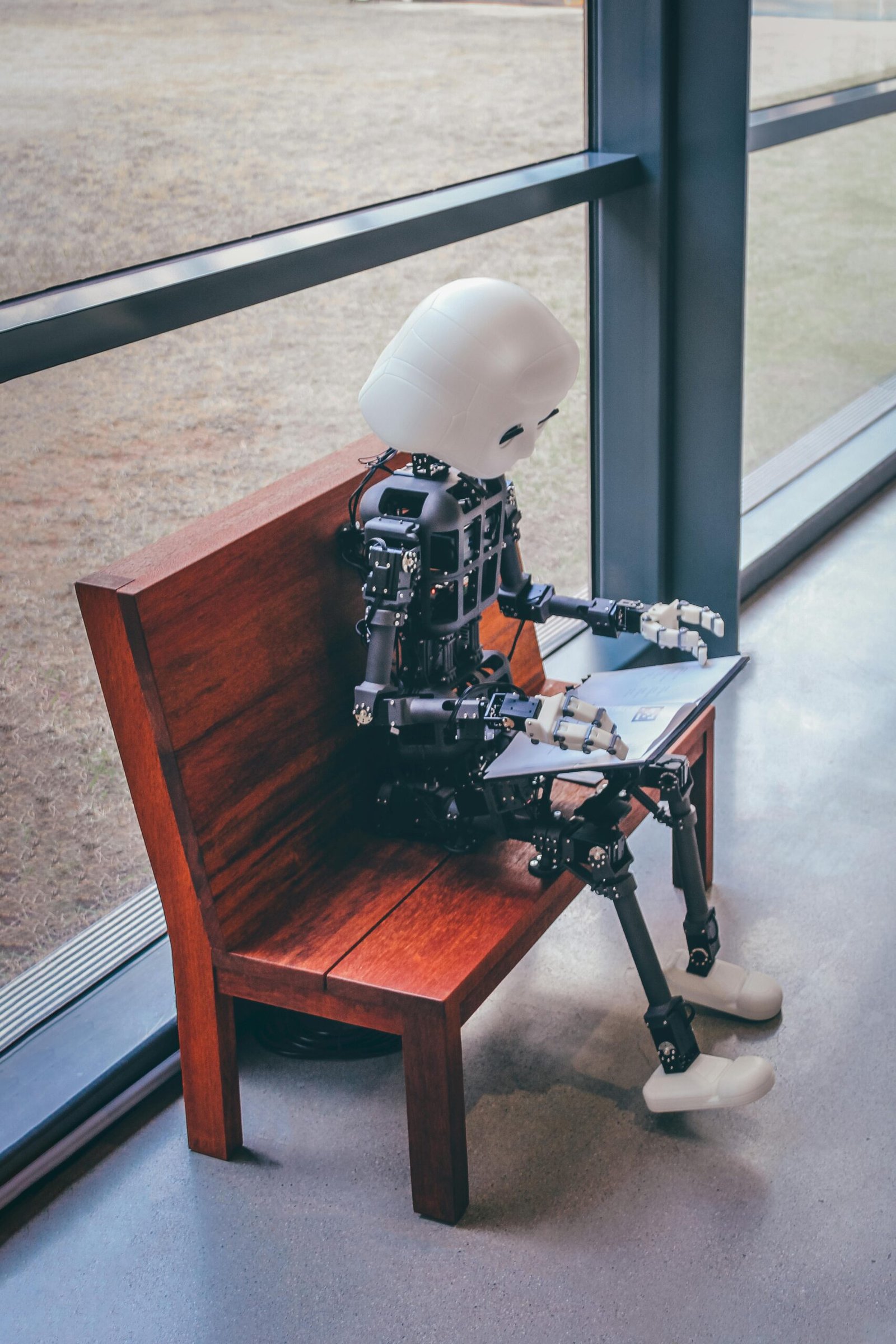 A humanoid robot sits on a wooden bench, reading in a modern setting in Seoul.
